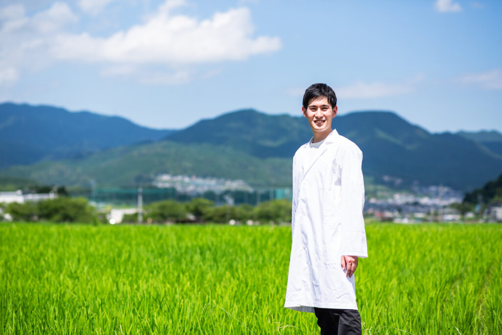 山並みを背景に田んぼに立つプロジェクトのつくり手